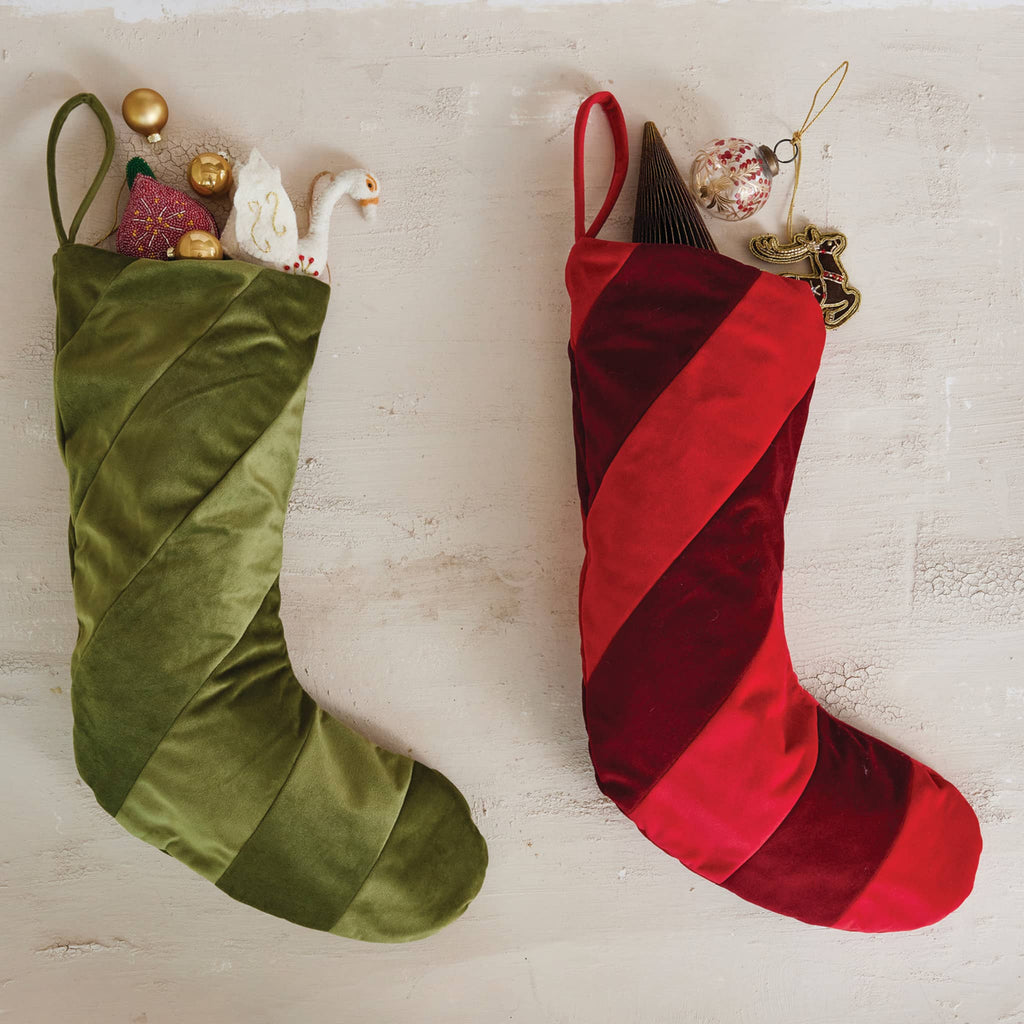 Green and red striped velvet Christmas stockings with decorative elements on a light wooden surface.