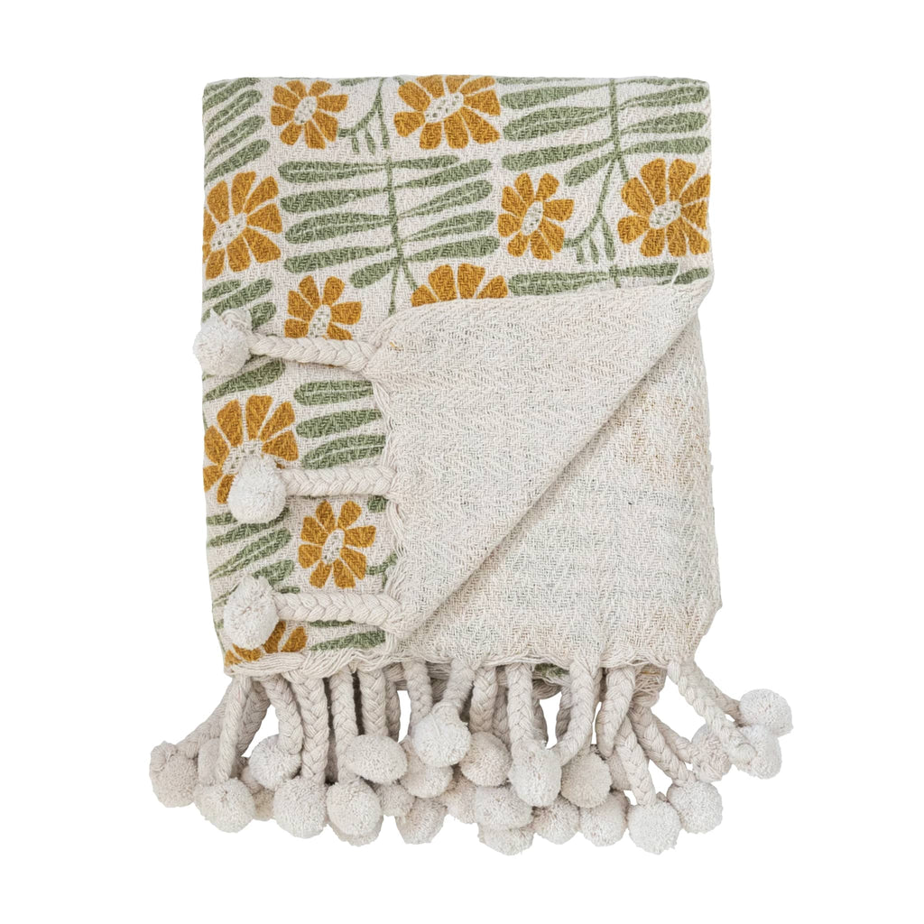 Creative Co-op woven recycled cotton blend mustard and sage floral print throw with braided pompom tassels, folded with corner flipped back to show solid reverse side.