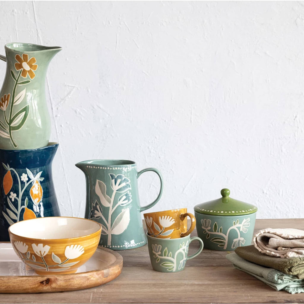 Creative Co-op 8 ounce hand-painted stoneware mugs in mustard and blue with wax relief flower design, stacked and shown with other items in the Buttercup Collection.