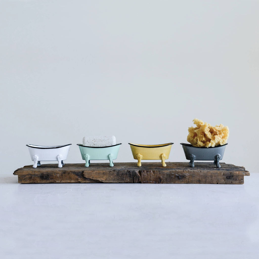 Creative Co-op metal enamel vintage bathtub soap dish in yellow, gray, mint green and white with a black rim lined up on a wood shelf with soap and a sponge.