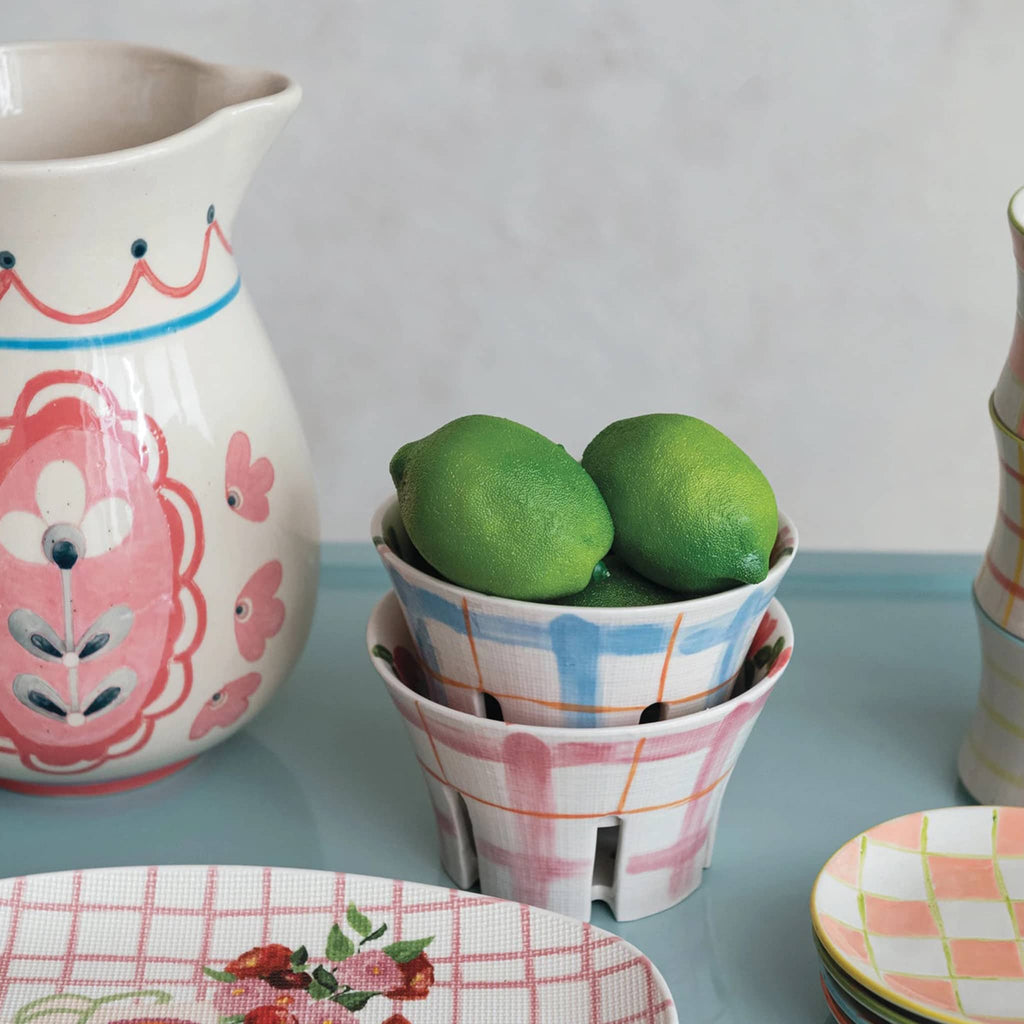 Creative Co-op hand-painted stoneware berry bowl with pink or blue plaid pattern on the outside, shown stacked with limes inside with other products from the collection.