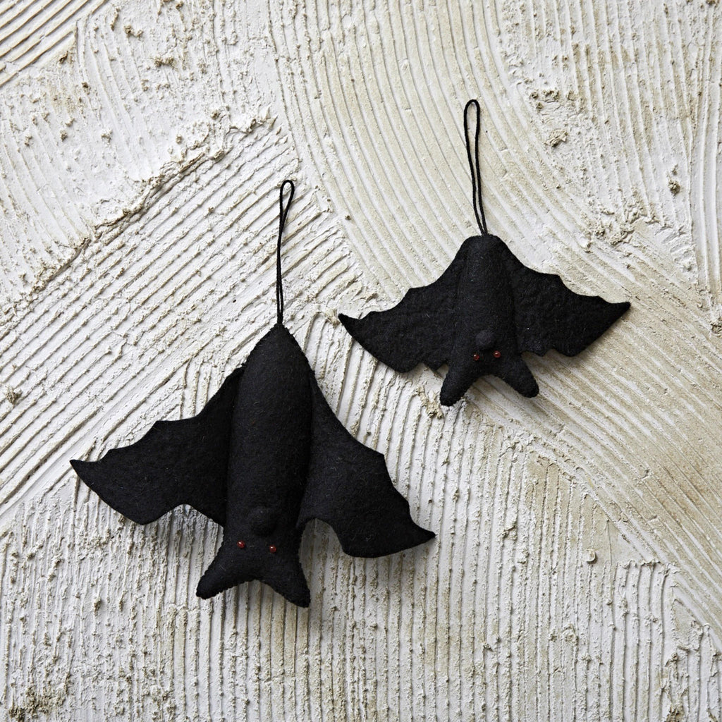 Creative Co-op Small and Large Handmade Black Wool Felt Hanging Bat Ornaments with red bead eyes, hanging on a stucco surface.