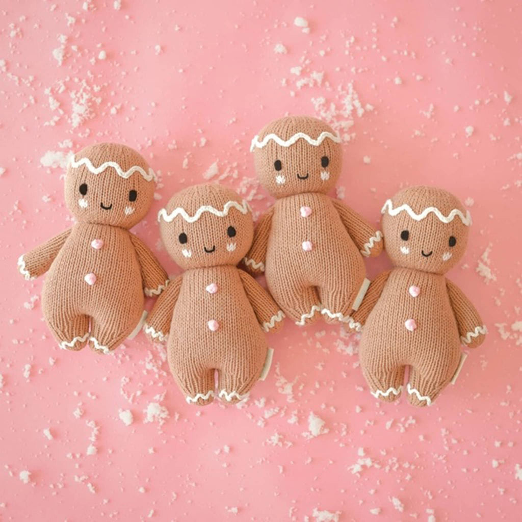 Four knitted gingerbread dolls on a pink background with white sprinkles.