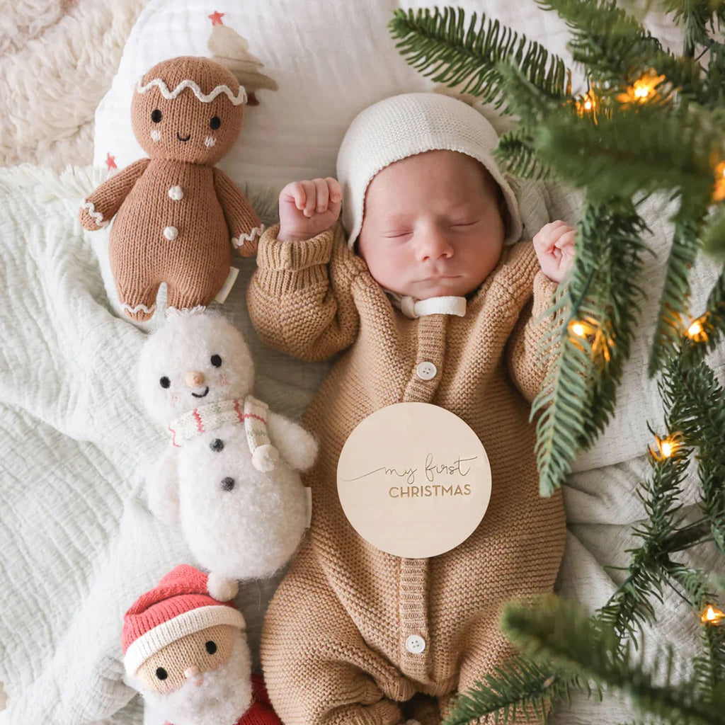 Newborn baby in a 'my first Christmas' outfit surrounded by Christmas-themed toys and decorations.