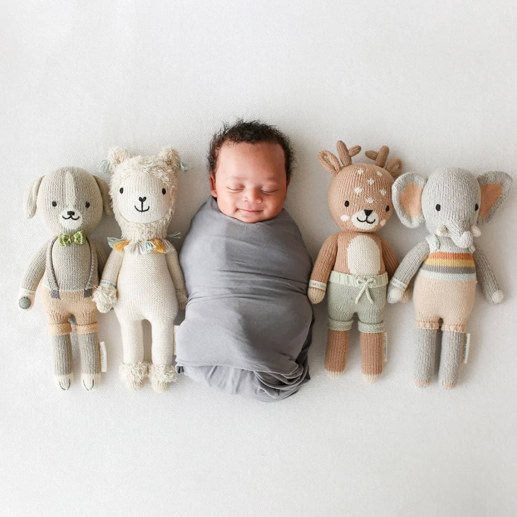 Newborn baby surrounded by four knitted toys on a white background.