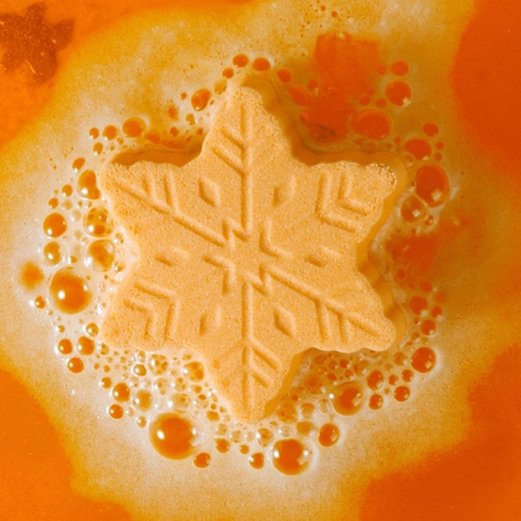 Snowflake-shaped orange bath fizzer with bubbles on a bright orange background.