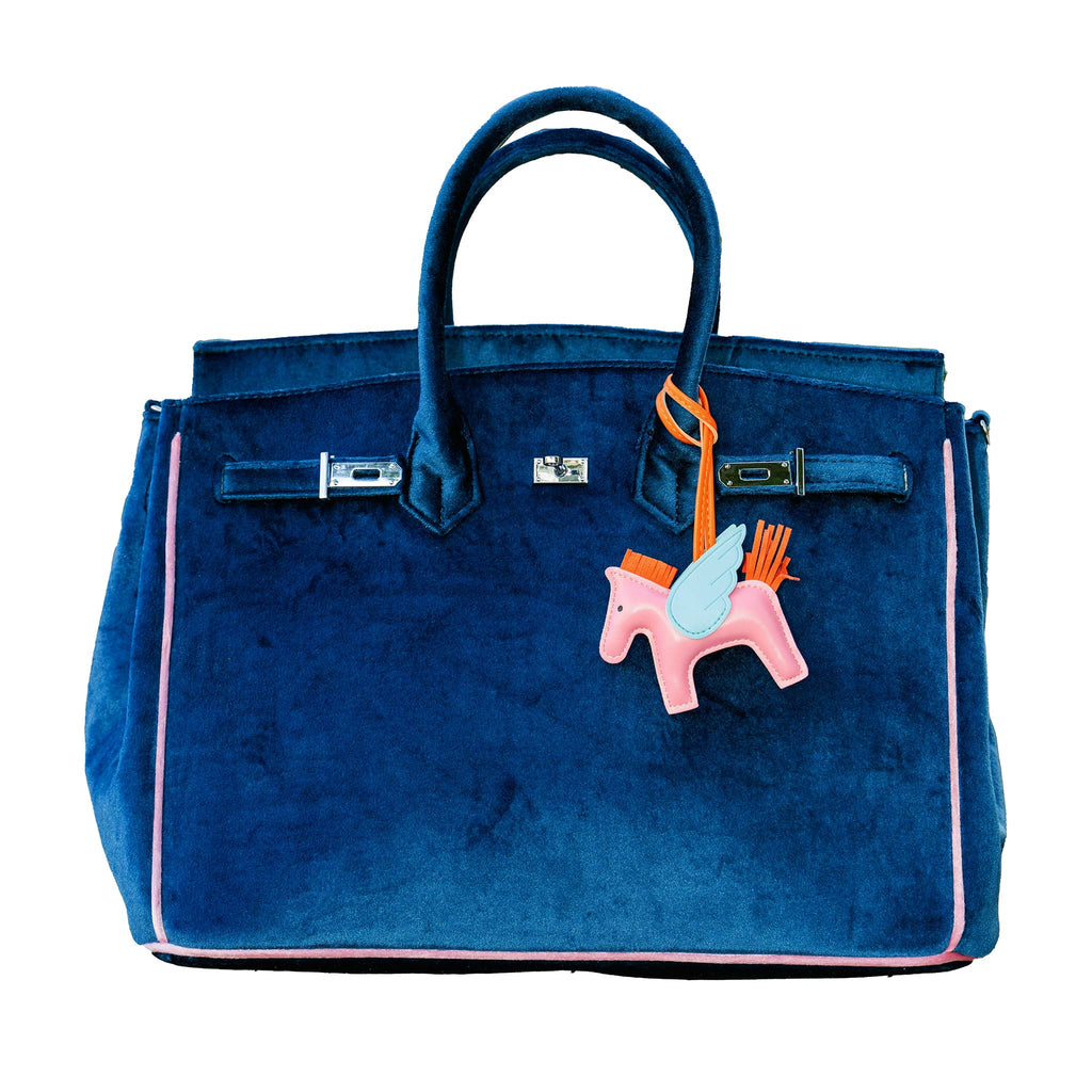 Blue velvet handbag with a pink horse charm on a white background.