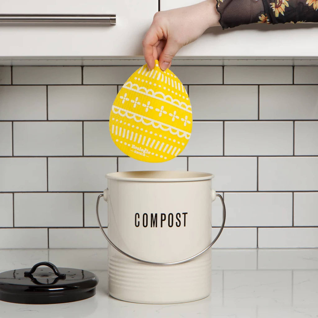 Danica Egg-Shaped Swedish Sponge Cloth in yellow, being placed in a compost bin to show size.