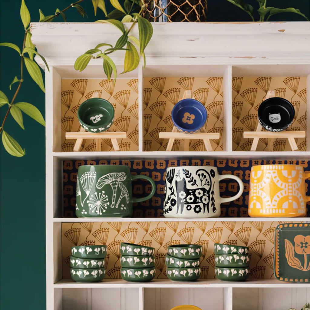 Shelf with patterned wallpaper displaying various mugs and bowls.