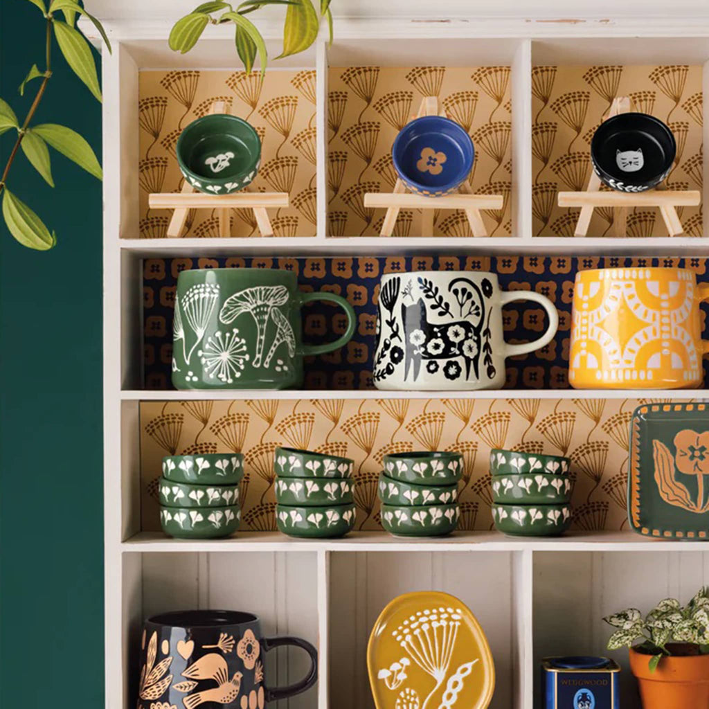 Shelf with patterned mugs and bowls against a green wall.