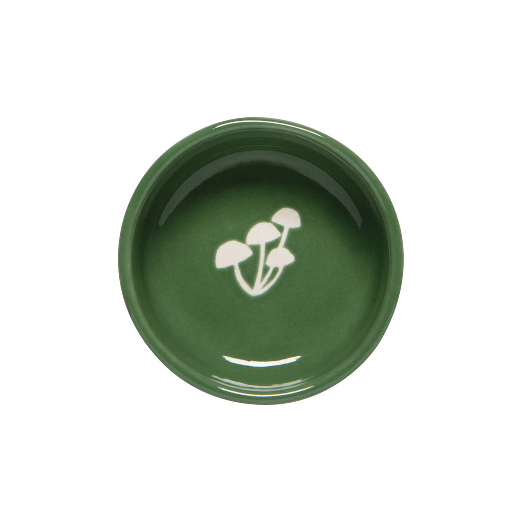 Small green ceramic dish with white mushroom wax-resist pattern on the bottom, overhead view, on a white background.