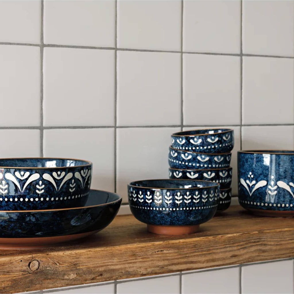 Set of blue ceramic bowls with white patterns on a wooden shelf against a tiled wall.