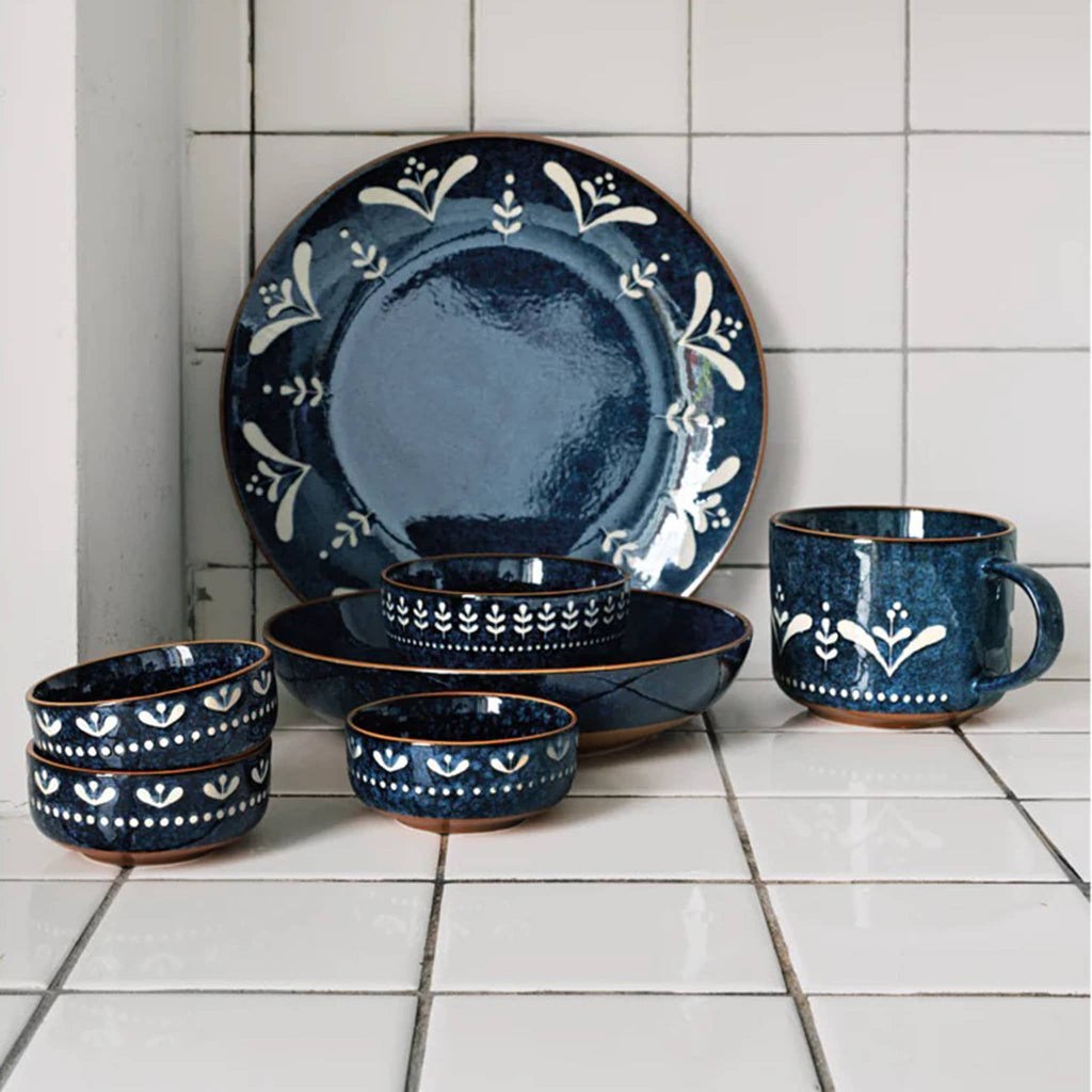Set of blue ceramic dinnerware with white floral patterns on white tile.
