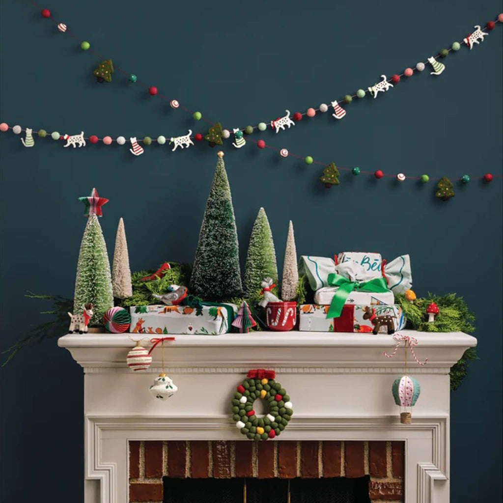 Decorated Christmas mantel with trees, presents, and ornaments against a dark green wall.