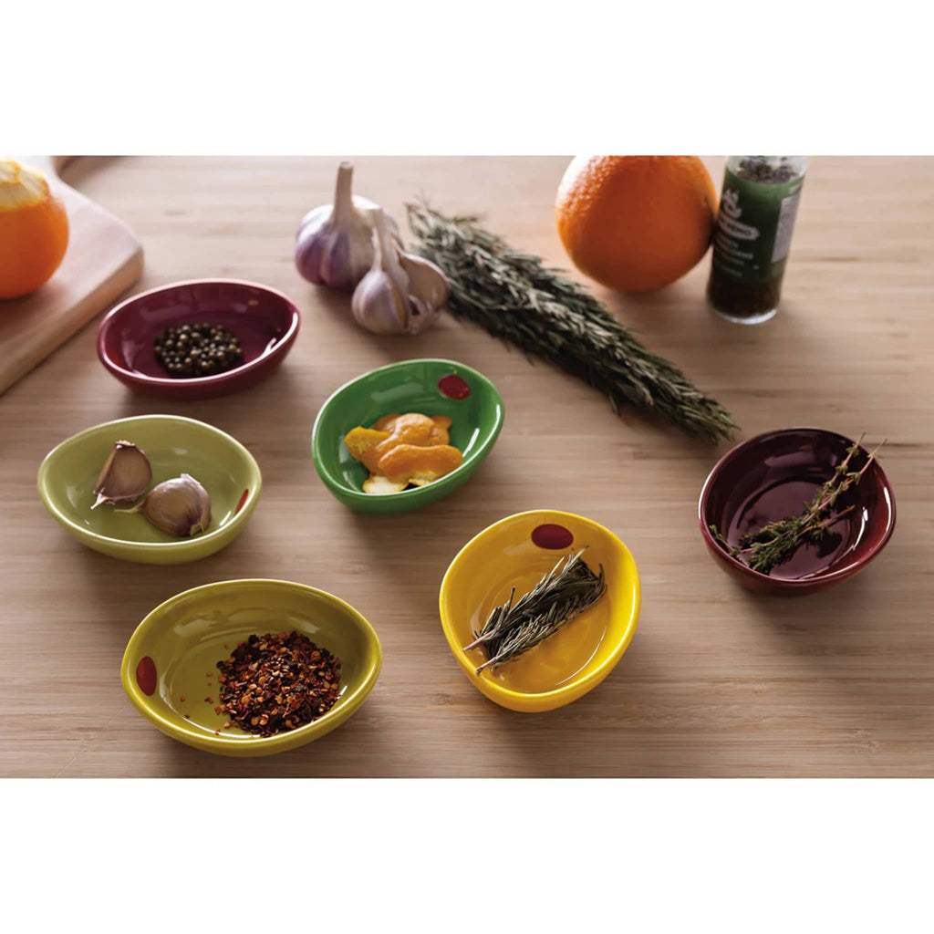 Set of six colorful ceramic olive-inspired pinch bowls filled with herbs and spices on a wood background.