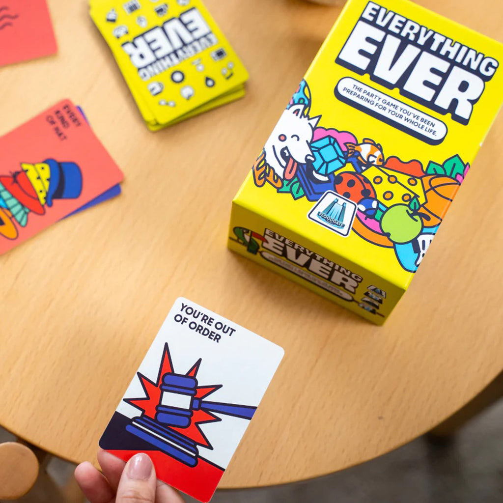 Dara Studios x Floodgate Games Everything Ever: the party game you've been preparing for your whole life, card game in yellow box packaging, front view, on table with hand holding the "you're out of order"  card.