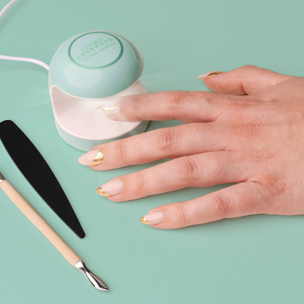 Green gel nail lamp with a hand and painted nails on a light green background.