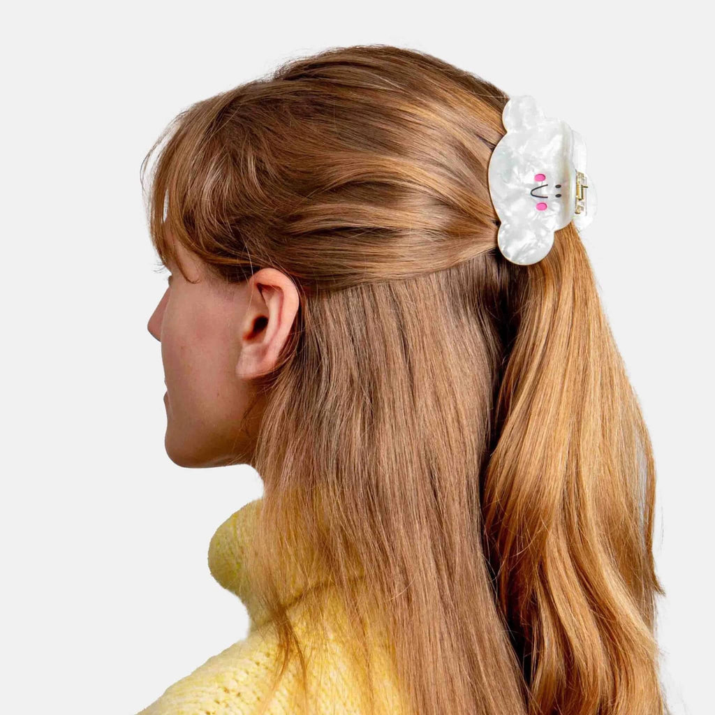 Woman with blonde hair tied in a ponytail with a decorative cloud hair clip on a white background.