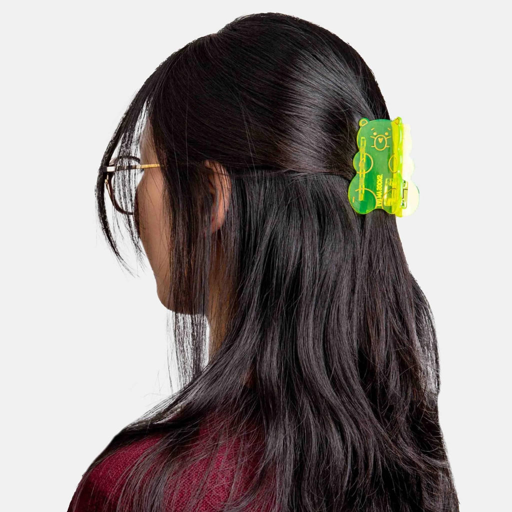 Person with long dark hair wearing a yellow gummy bear-shaped plastic hair claw on a white background.