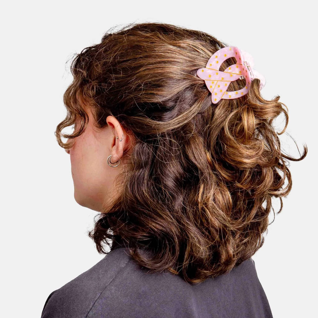 Person with curly hair wearing a pink pretzel hair clip on a white background.