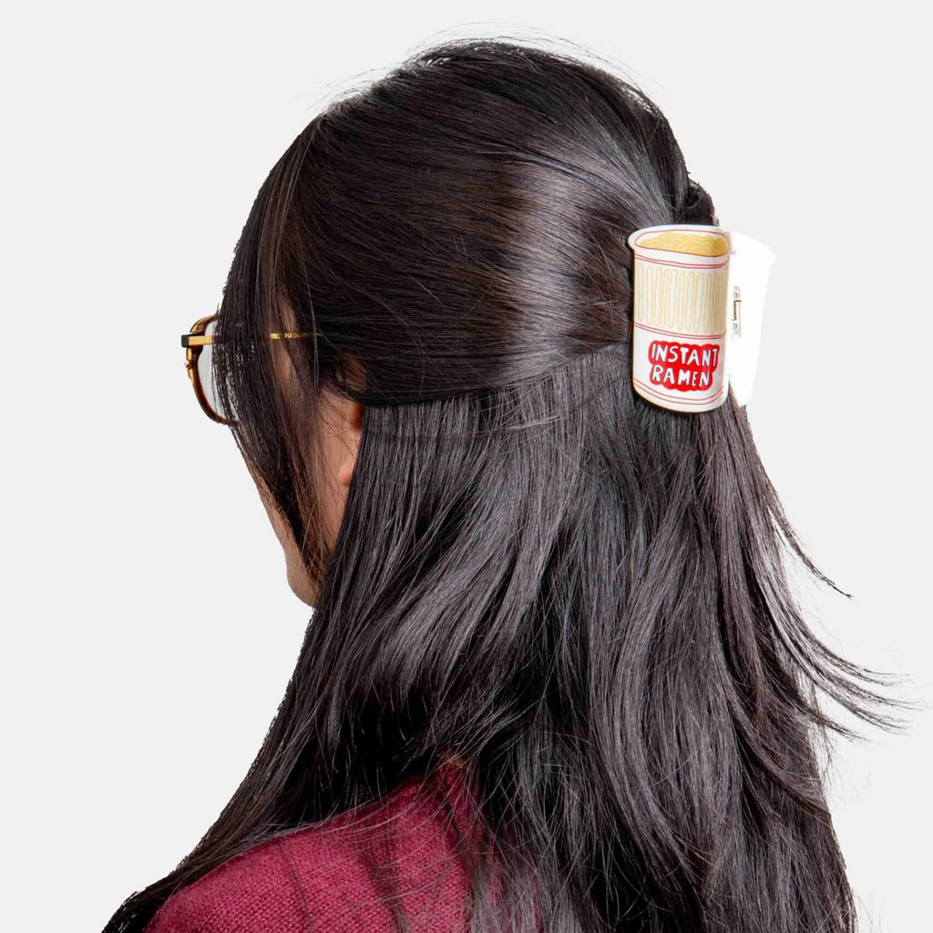 Person with a 'Instant Ramen' themed hair clip in their hair on a white background.