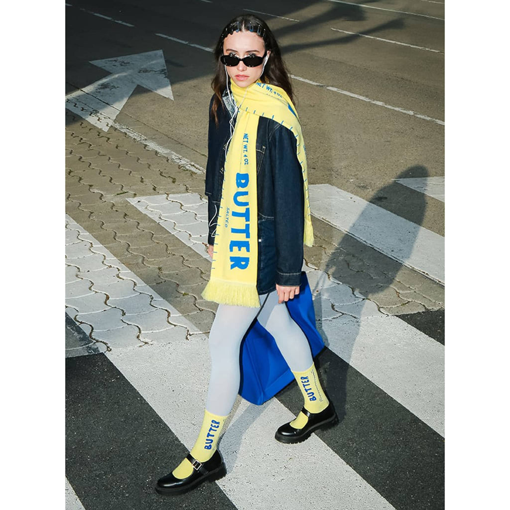 Person wearing yellow butter scarf and matching socks, walking in a crosswalk.