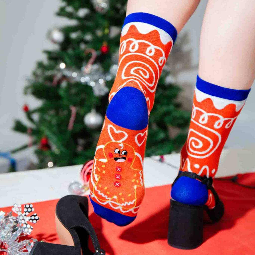 Person wearing festive gingerbread-themed socks with a Christmas tree in the background.