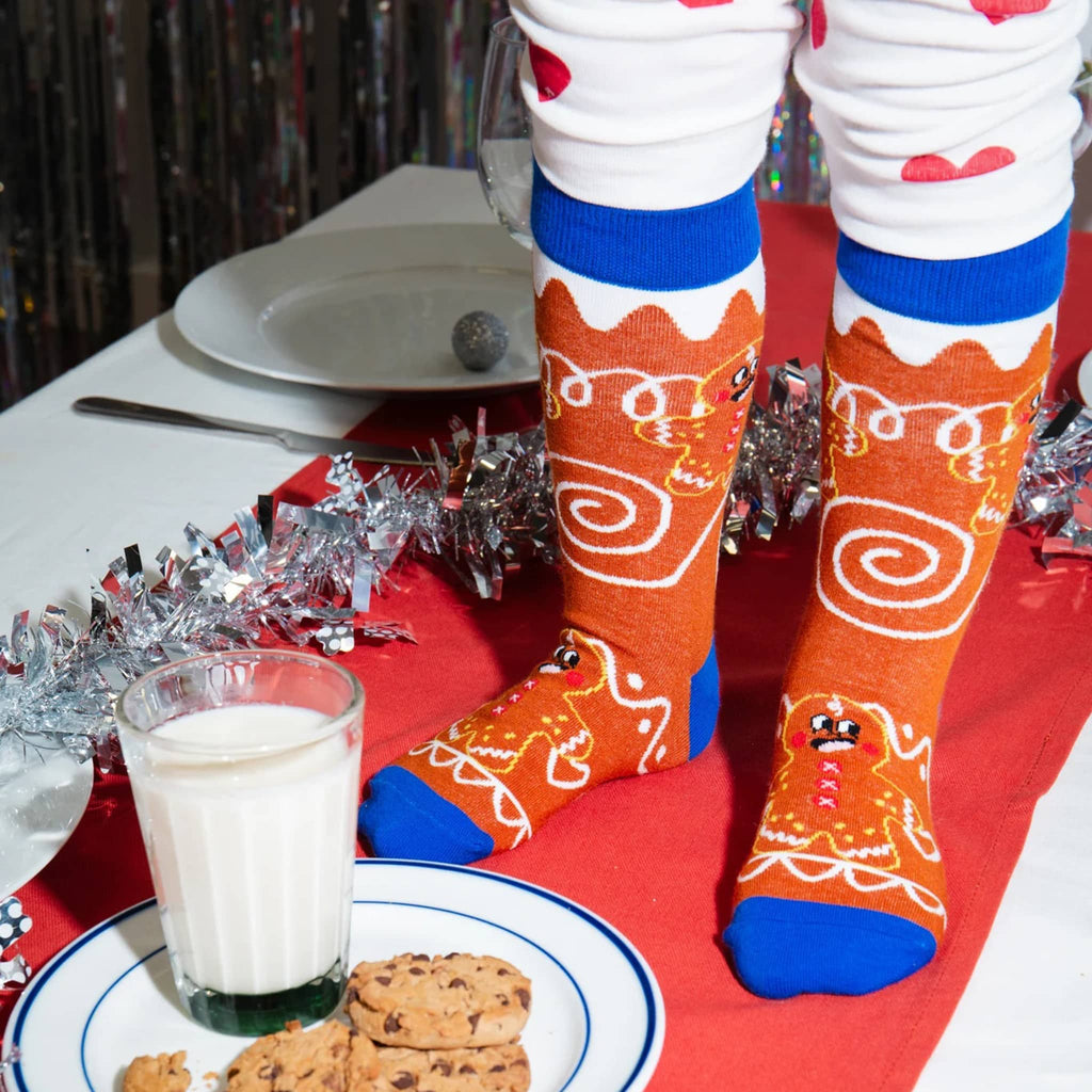 Person wearing festive socks with gingerbread design at a table with cookies and milk.