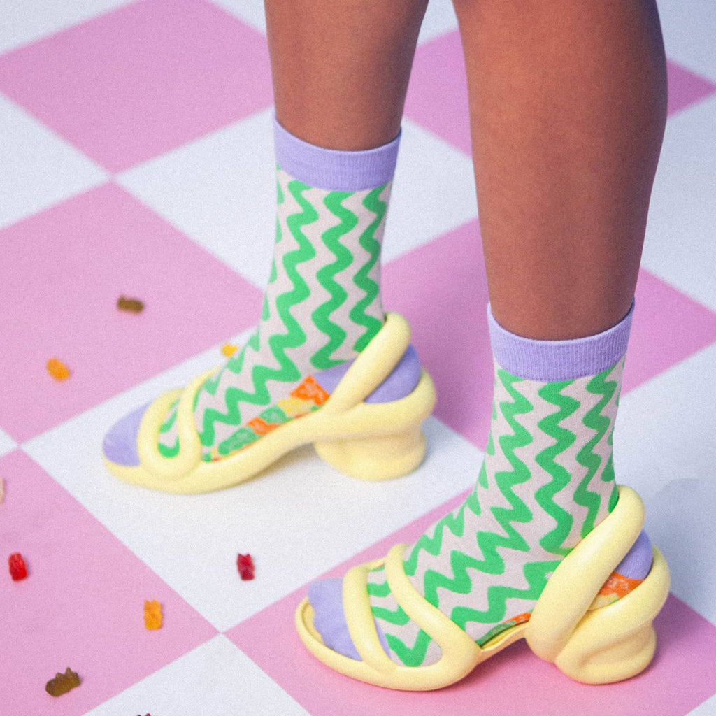 Person wearing green zigzag pattern socks with purple accents on a pink checkered floor.