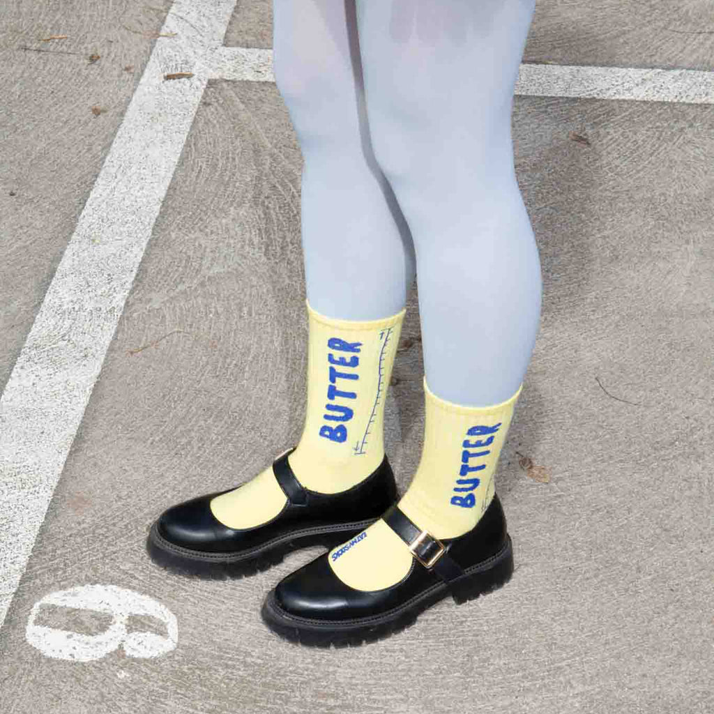Person wearing yellow socks with 'BUTTER' text, black shoes, and light blue tights on a street.