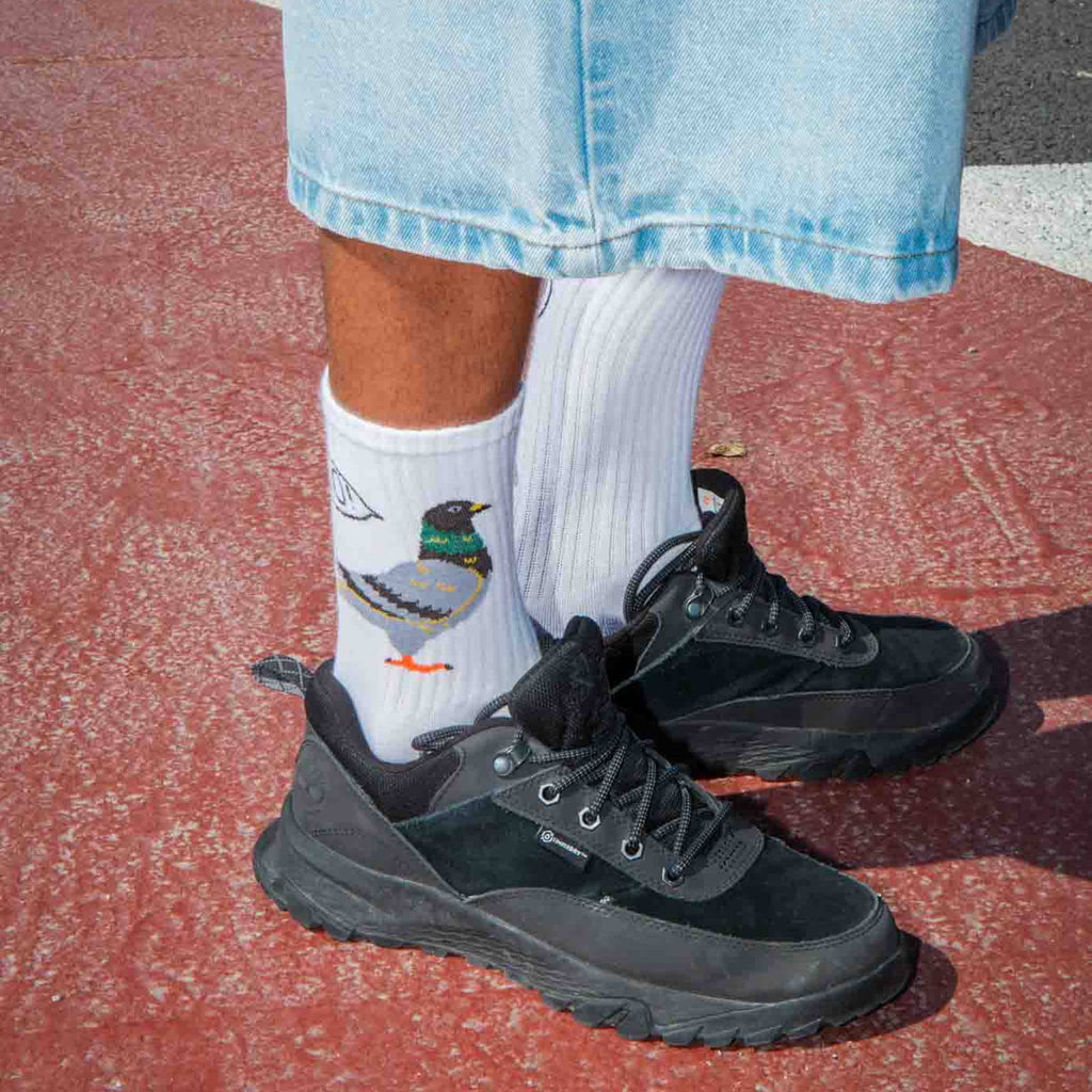 Person wearing black sneakers and white socks with a pigeon design on a red-paved surface.