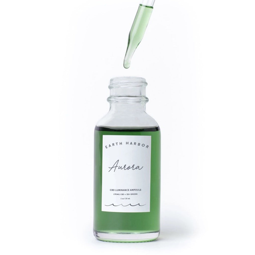 Earth Harbor Aurora Superfood Luminance Ampoule in 1 ounce clear glass bottle with eyedropper dripping green elixir into bottle.