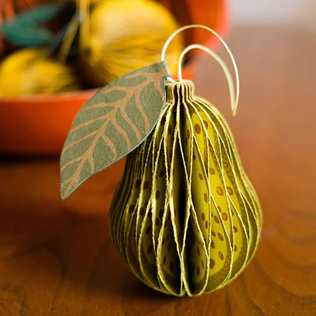 Decorative green pear-shaped honeycomb paper ornament with a leaf on a wooden surface.
