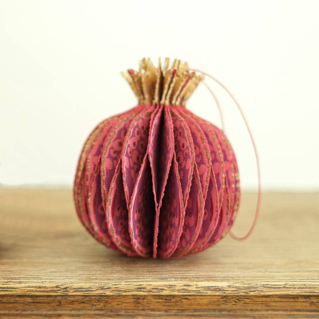 Decorative red pomegranate-shaped honeycomb paper ornament on a wooden surface with blurred background.