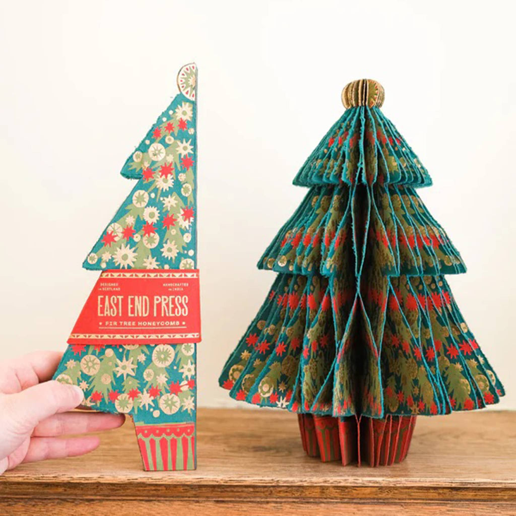 Paper Christmas tree with star patterns on a wooden surface with flat version in packaging next to it.