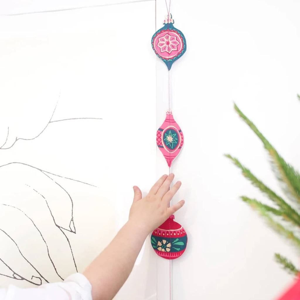 Colorful hanging decorative item with a child's hand reaching out to touch it against a white background.