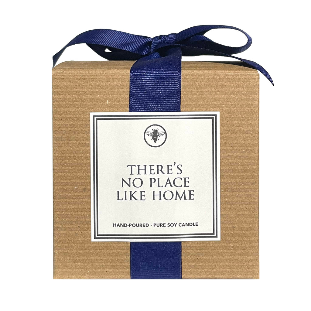 Ella B Candles "There's No Place Like Home" sandalwood and cashmere scented soy wax candle in brown kraft paper box with navy blue grosgrain ribbon, front view.