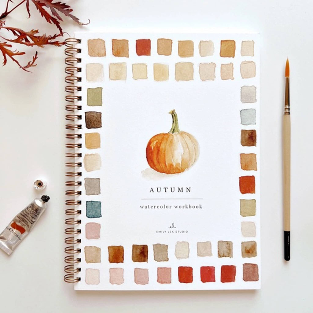 Autumn-themed watercolor workbook with color swatches and a pumpkin illustration, surrounded by art supplies on a white background.