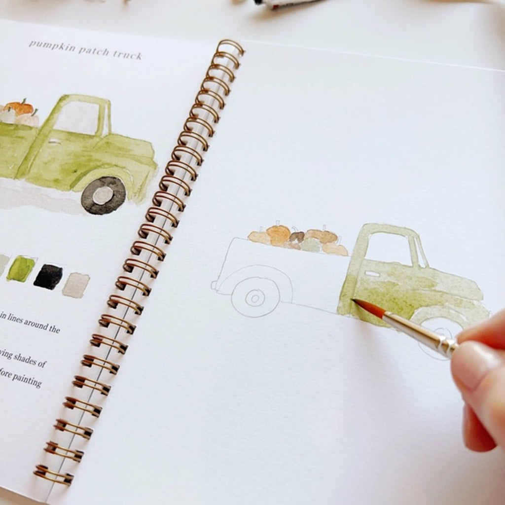 Person painting a green truck illustration on a notebook with a paintbrush.