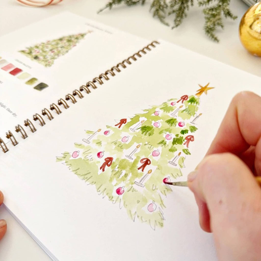 Person coloring a Christmas tree on a notebook with a watercolor brush.