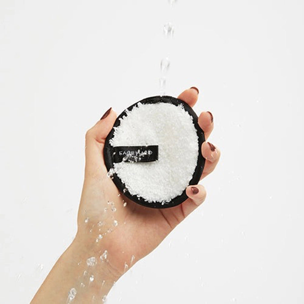 Face Halo Original Reusable Microfiber Makeup Remover Pad in palm of hand with water splashing on it.