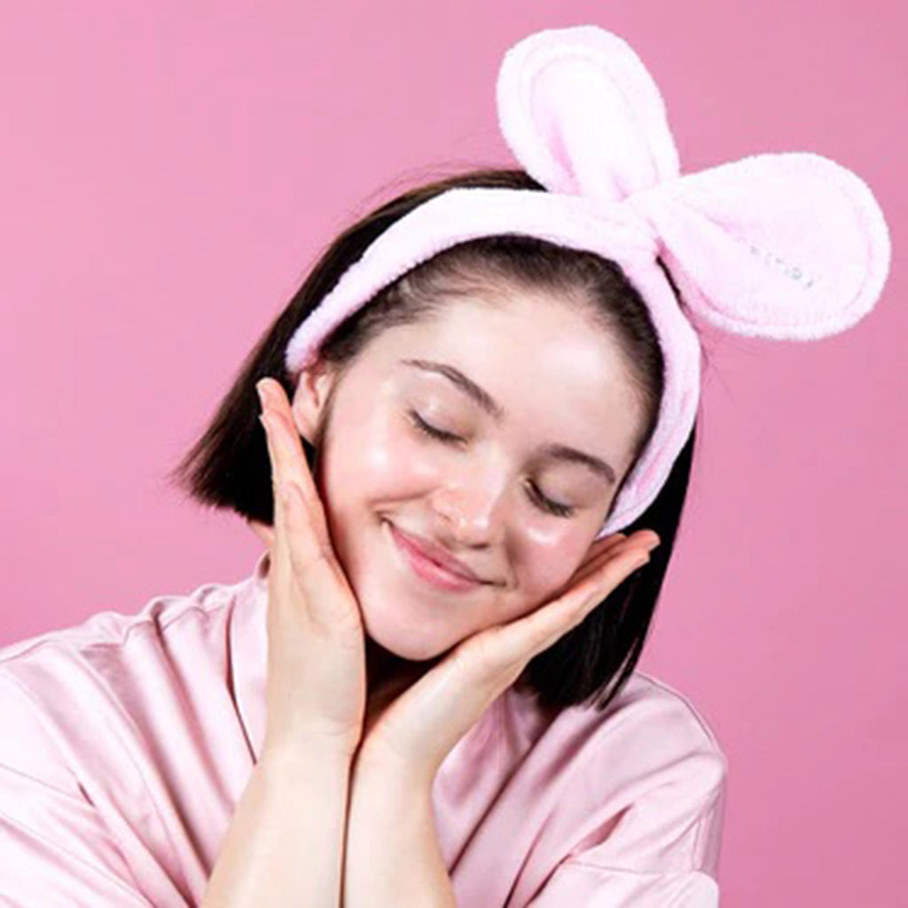 Facetory Tory Twist Bunny Hair Band in blush pink with logo on one "ear" in use on a model who is wearing a pink satin robe on a pink background.