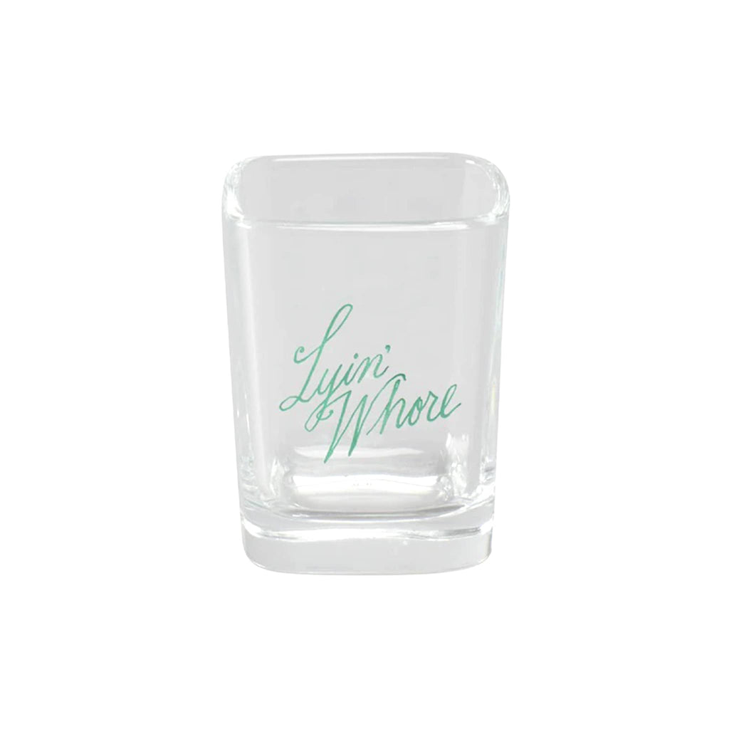 Clear shot glass with "Lyin' Whore" in green text, on a white background.