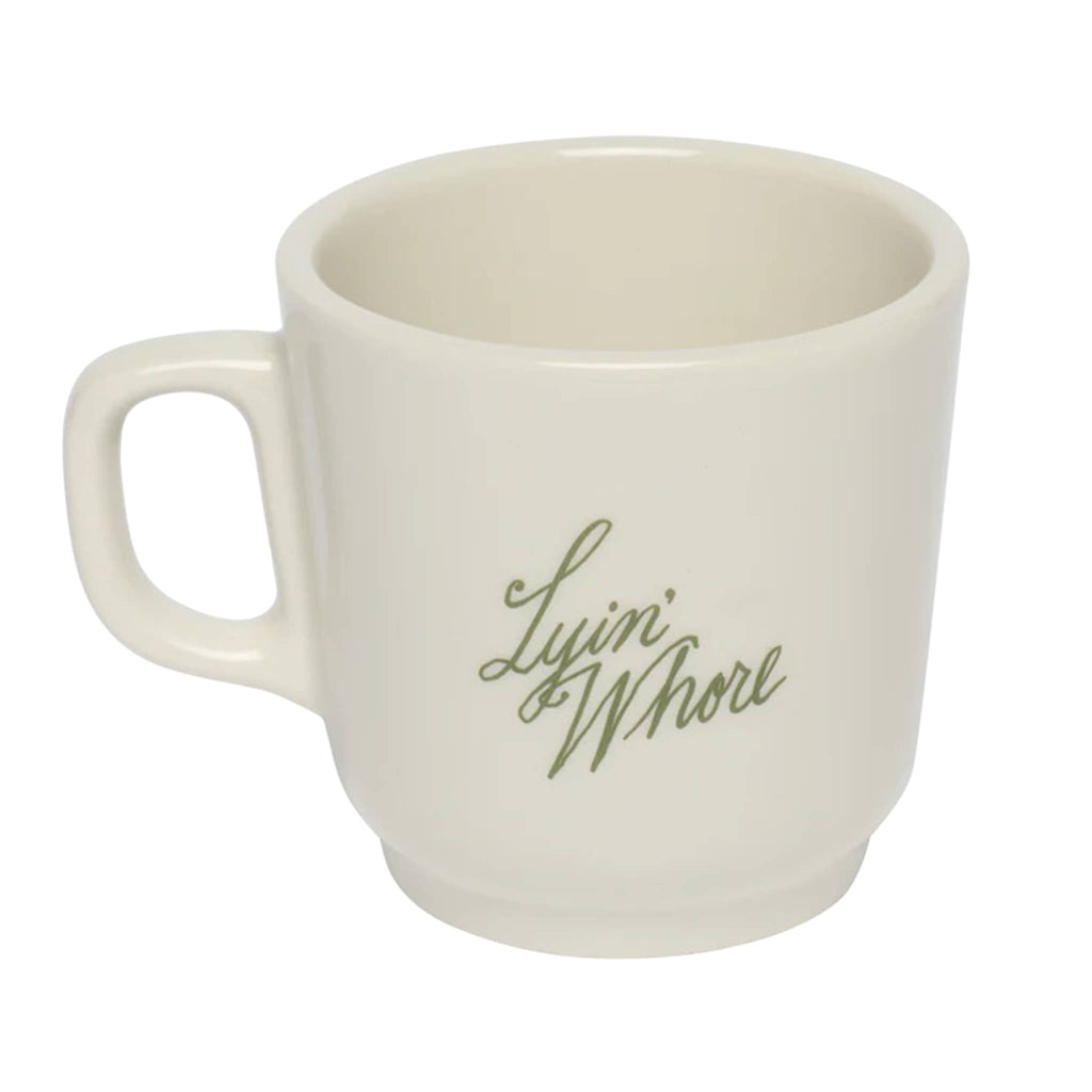 White mug with "Lyin' Whore" in green text, on a white background, slight overhead view.