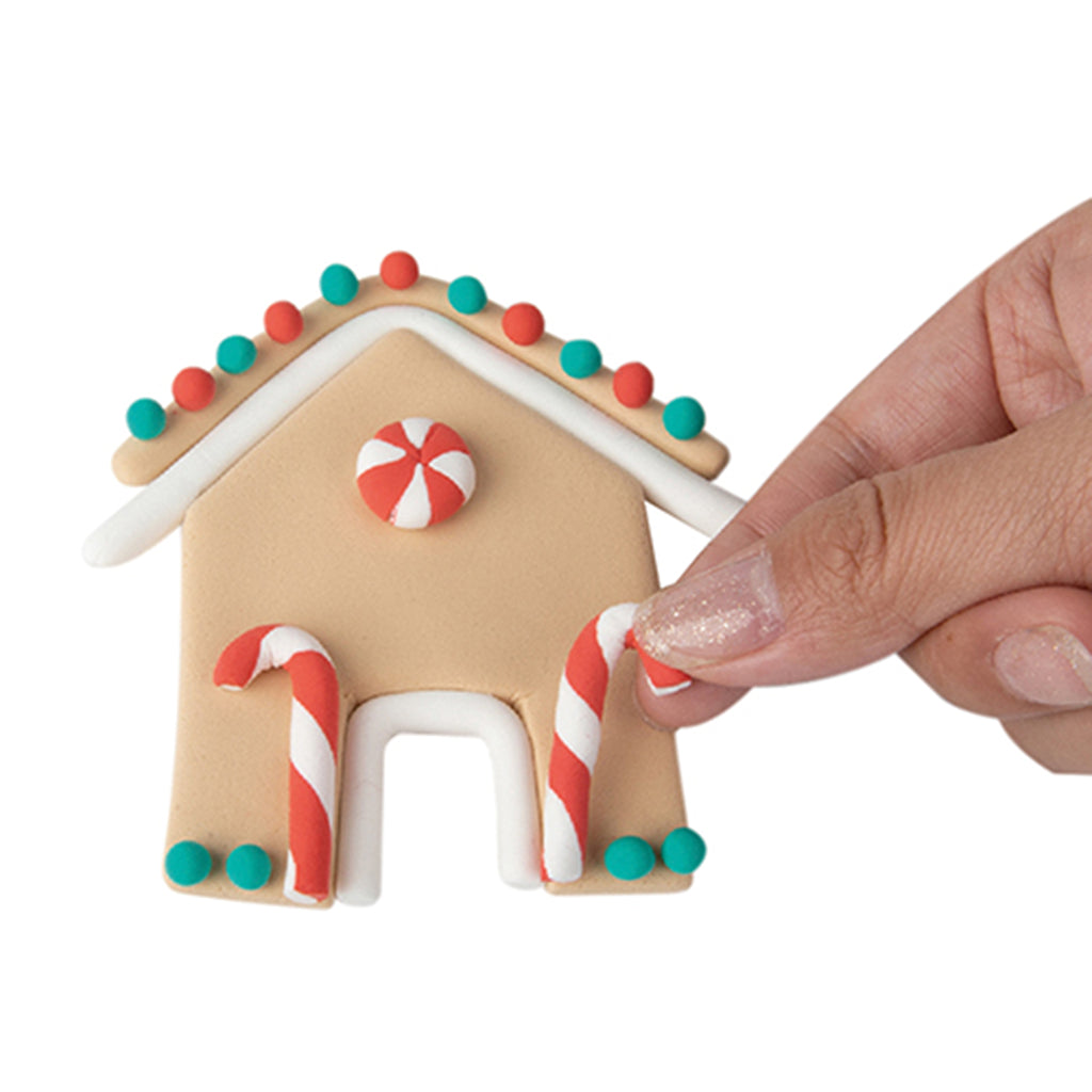 Fizz Creations Make Your Own Gingerbread House modeling dough kit, hand placing candy cane on house.