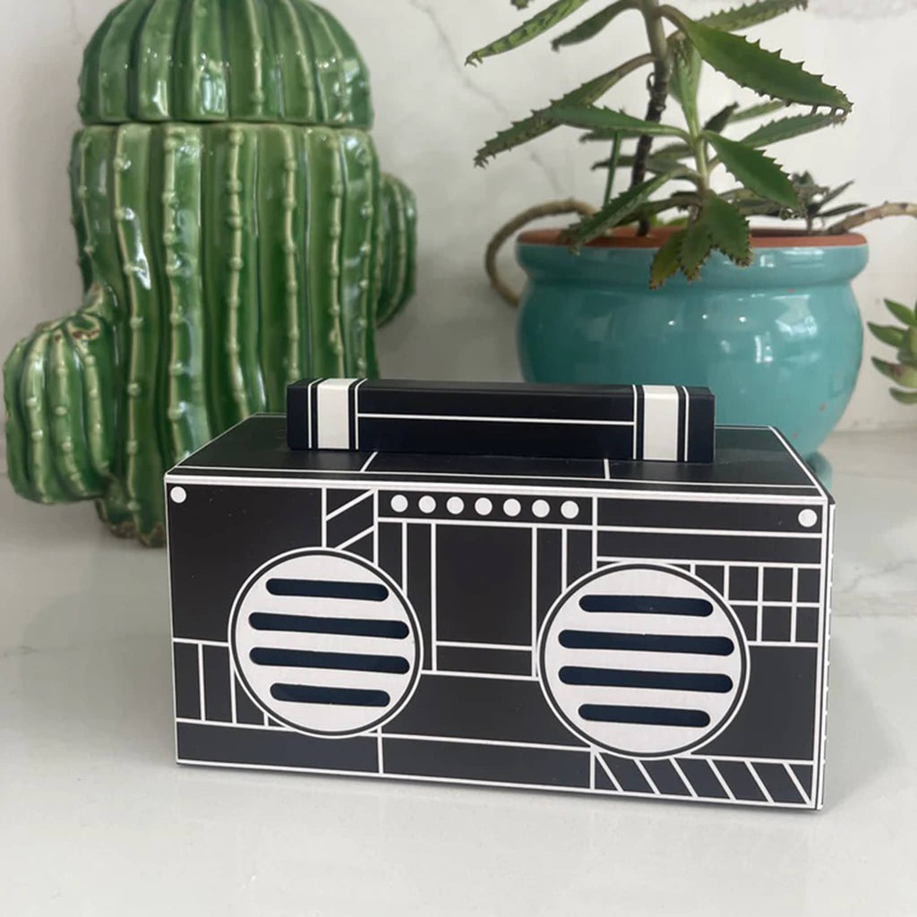 Funky Rico black and white retro boombox wireless speaker, front angle view, with plant and cactus jar in background.