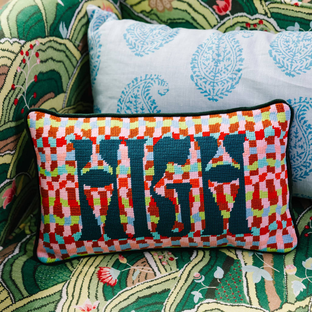 Colorful needlepoint pillow with geometric pattern and "HIGH" in dark green lettering, shown on a patterned chair with another pillow.