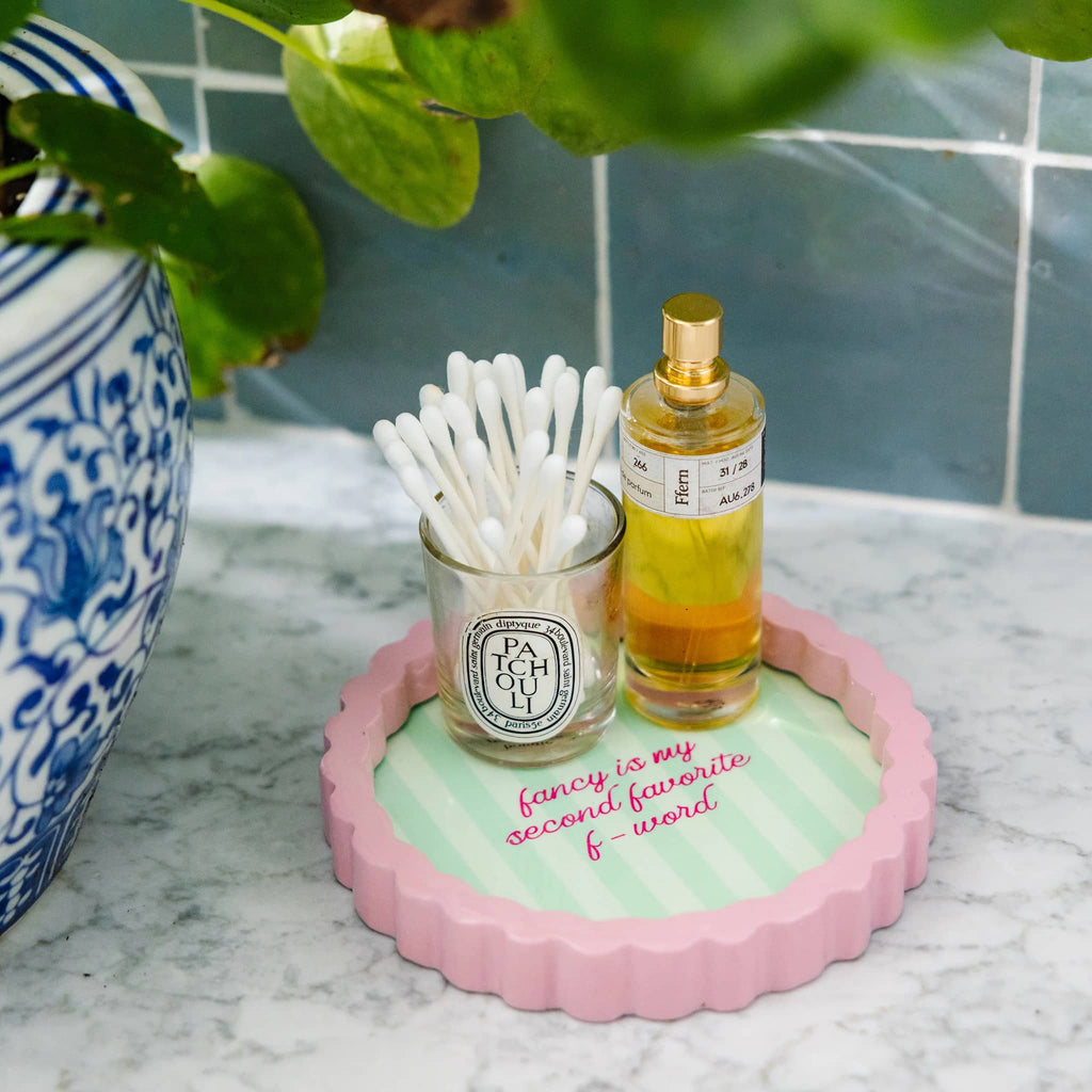 Small round tray with cotton swabs and a bottle of perfume on a marble surface.