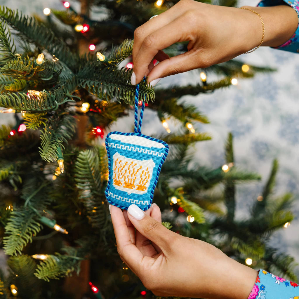 Hand holding a greek coffee cup Christmas ornament against a decorated tree background.