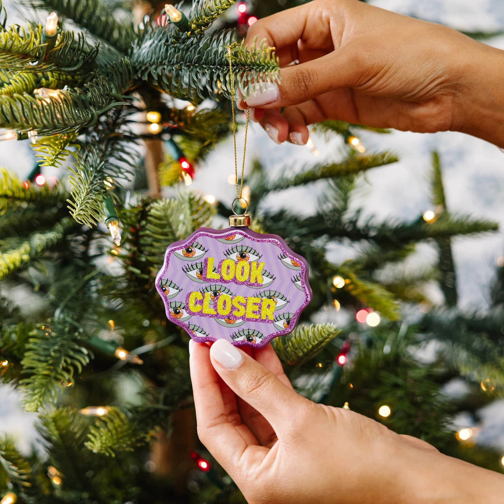 Hand holding a decorative ornament with 'Look Closer' text on a Christmas tree.